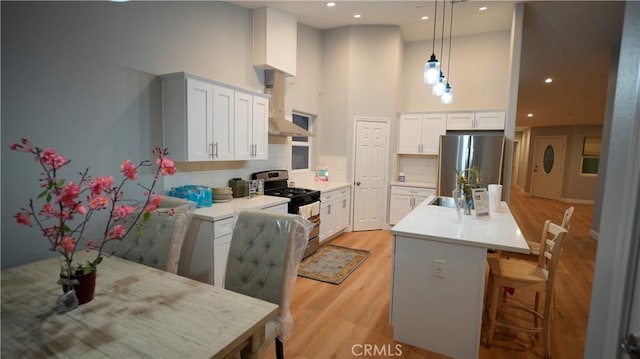 14610 Appleton St, Hesperia, CA 92345 - kitchen featuring stainless steel appliances, wall chimney exhaust hood, a towering ceiling, tasteful backsplash, and light wood-type flooring