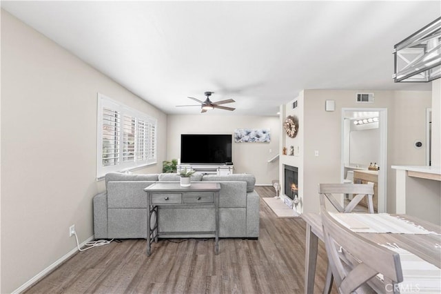 living room featuring baseboards, a lit fireplace, visible vents, a ceiling fan, and wood finished floors