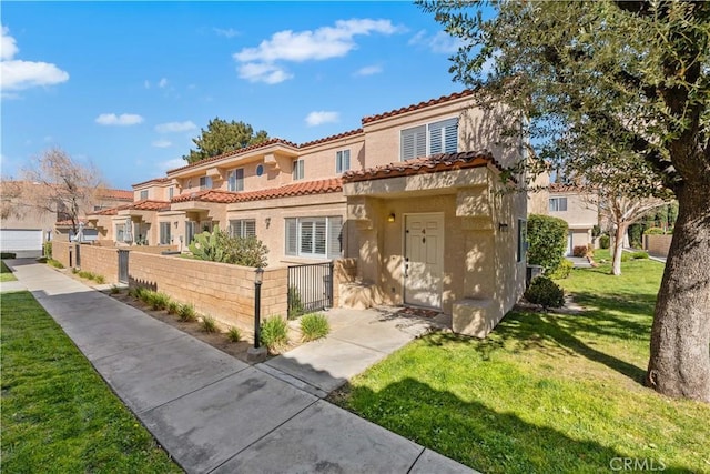 mediterranean / spanish home with a front lawn, a tile roof, a fenced front yard, and stucco siding