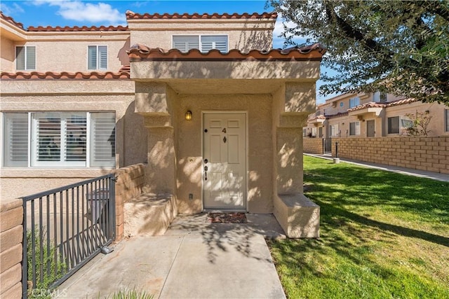 property entrance with stucco siding, a tile roof, fence, and a yard