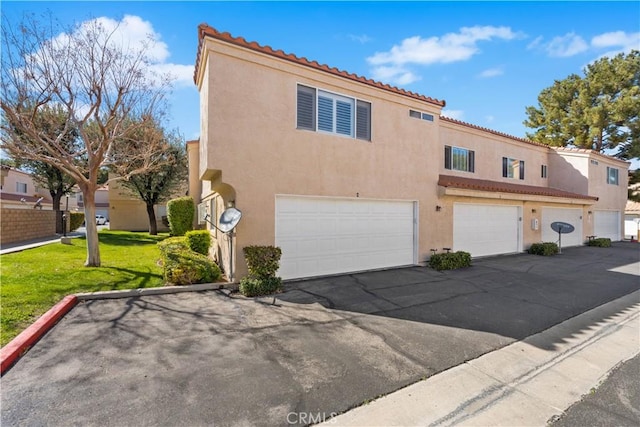 view of front of property featuring driveway, a front yard, stucco siding, a tiled roof, and a garage