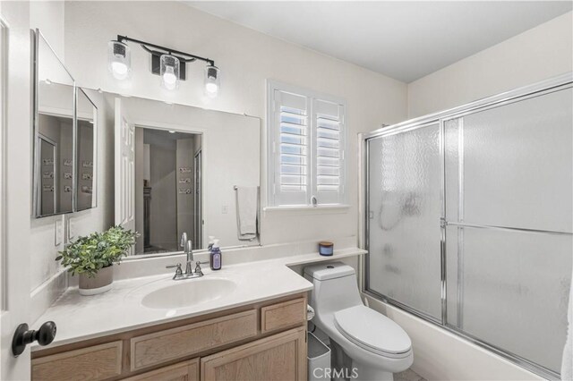 bathroom featuring toilet, shower / bath combination with glass door, and vanity