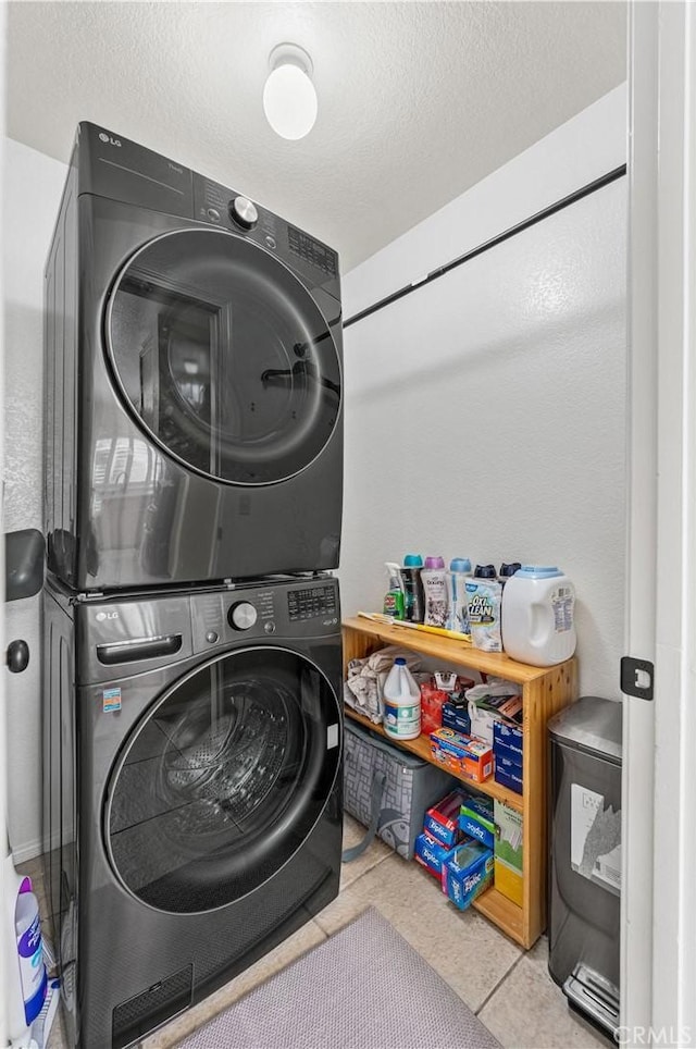 clothes washing area featuring tile patterned floors, stacked washer and clothes dryer, laundry area, and a textured ceiling