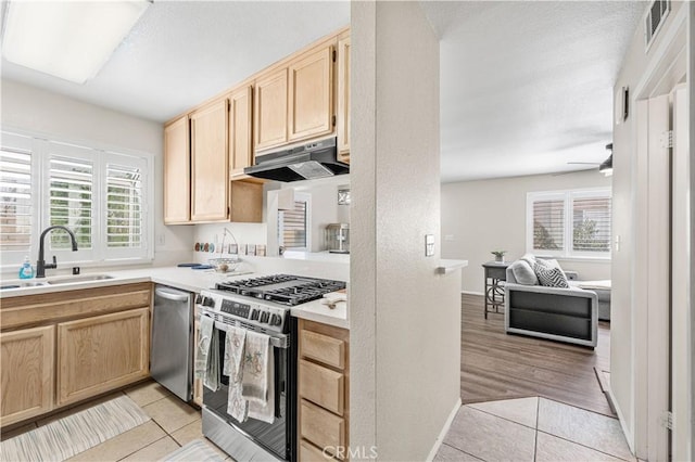 kitchen featuring light brown cabinetry, stainless steel appliances, under cabinet range hood, a sink, and light tile patterned floors