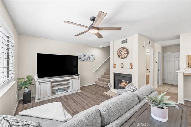 living room featuring a large fireplace, visible vents, baseboards, ceiling fan, and wood finished floors
