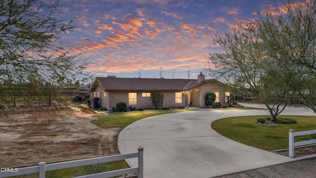 view of front facade with stucco siding, a fenced front yard, curved driveway, and a yard