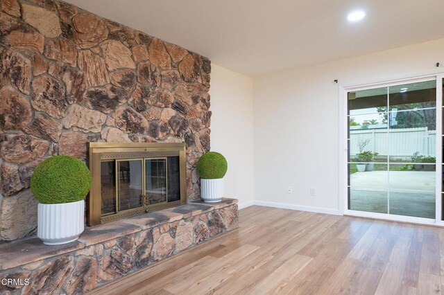 unfurnished living room with a stone fireplace, baseboards, and wood finished floors