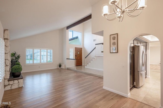 unfurnished living room featuring stairway, light wood-type flooring, an inviting chandelier, baseboards, and arched walkways