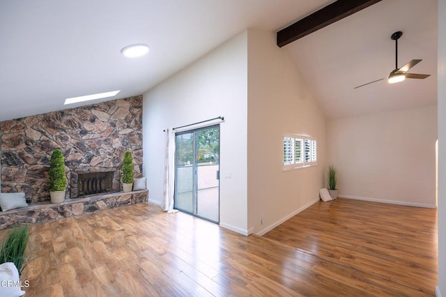 unfurnished living room with high vaulted ceiling, beam ceiling, ceiling fan, a fireplace, and wood finished floors