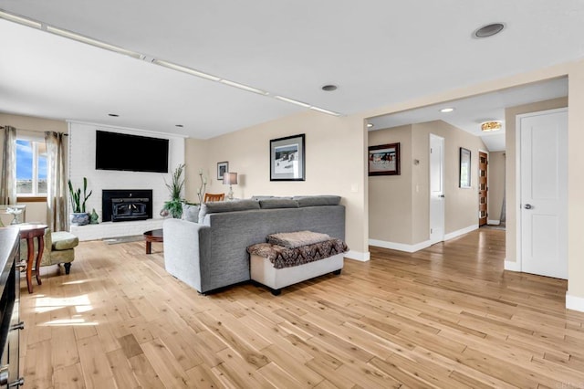 living room featuring recessed lighting, baseboards, a brick fireplace, and light wood-type flooring