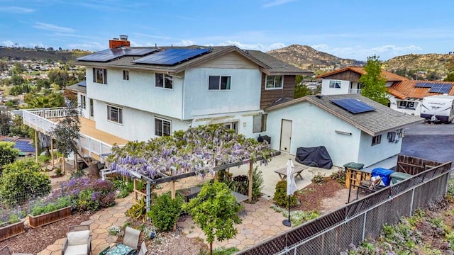 rear view of property with a fenced backyard, a mountain view, a chimney, roof mounted solar panels, and a patio