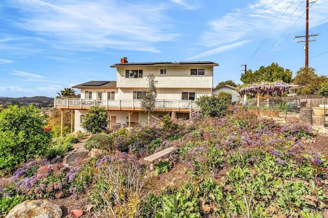 back of property with stucco siding, solar panels, a chimney, and a wooden deck