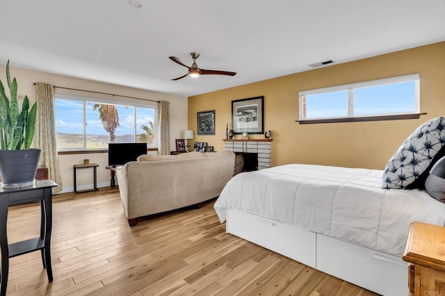 bedroom featuring light wood-style flooring, visible vents, a ceiling fan, and a brick fireplace