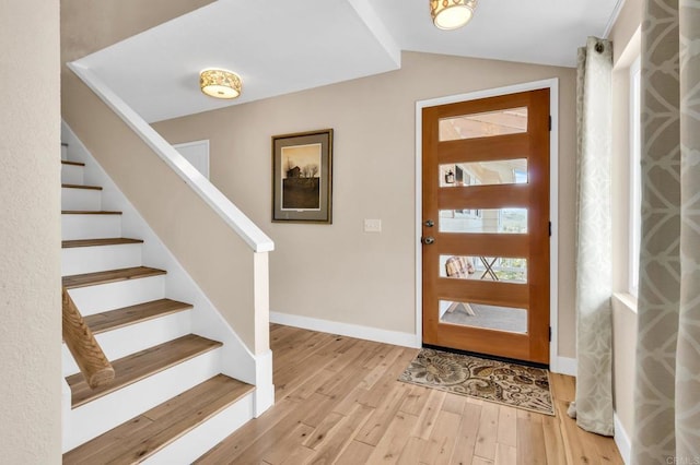 foyer featuring lofted ceiling, stairs, light wood finished floors, and baseboards