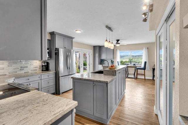 kitchen with a sink, freestanding refrigerator, backsplash, gray cabinetry, and an island with sink
