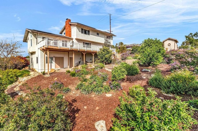 rear view of property featuring a wooden deck, a chimney, and stucco siding