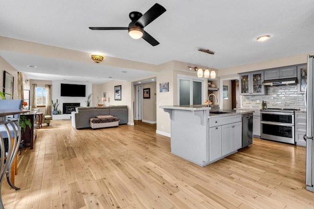 kitchen with a sink, tasteful backsplash, double oven range, under cabinet range hood, and a breakfast bar area