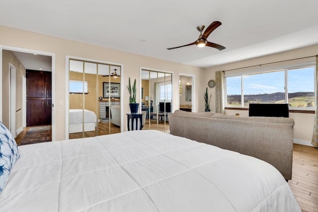 bedroom with a ceiling fan, wood finished floors, ensuite bathroom, multiple closets, and baseboards