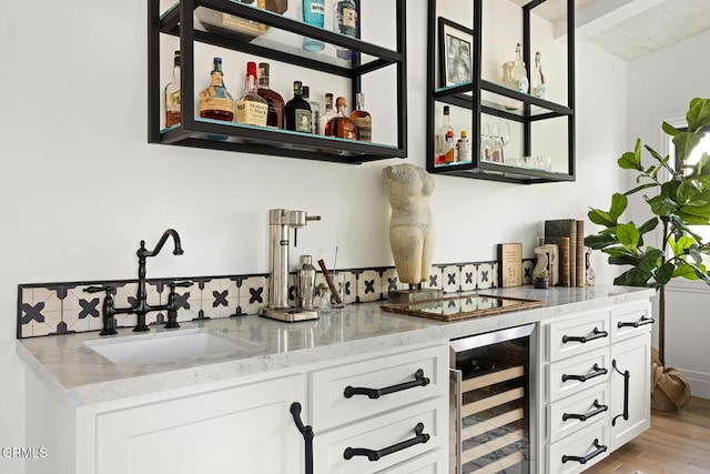 bar with wet bar, cooktop, a sink, light wood finished floors, and beverage cooler
