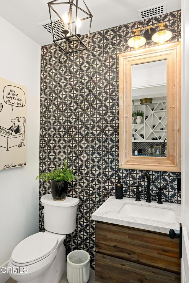 bathroom featuring vanity, toilet, decorative backsplash, visible vents, and a notable chandelier