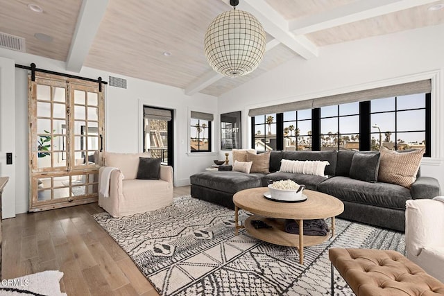 living room with visible vents, a barn door, wood finished floors, and lofted ceiling with beams