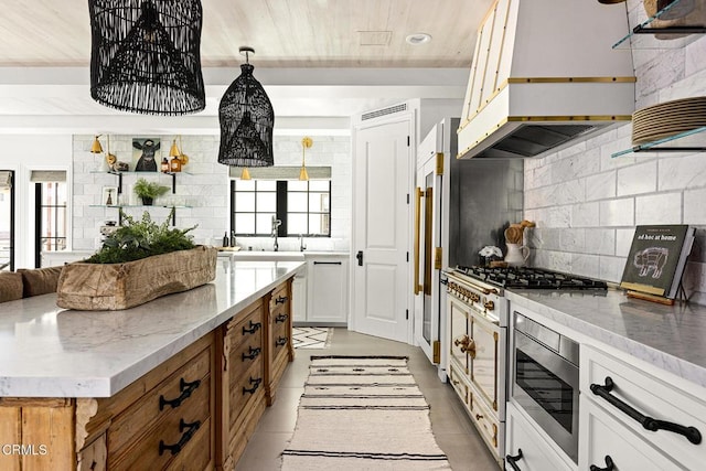 kitchen featuring stainless steel microwave, light stone counters, custom range hood, and tasteful backsplash