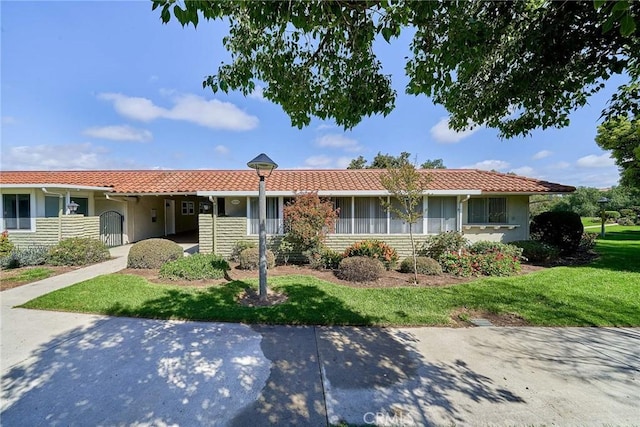 ranch-style house featuring a tile roof, a front yard, and stucco siding