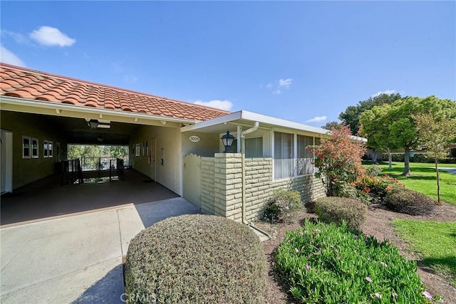 view of side of property featuring driveway, a tile roof, an attached carport, and stucco siding