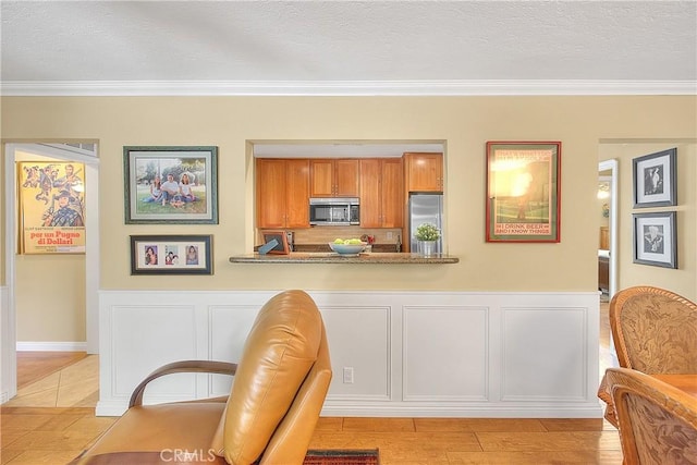 kitchen with brown cabinets, crown molding, a decorative wall, and stainless steel appliances
