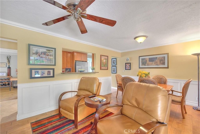living room with a textured ceiling, light wood-style floors, ornamental molding, and a ceiling fan