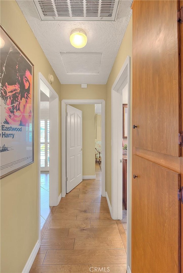 corridor featuring baseboards, light wood-style flooring, and a textured ceiling