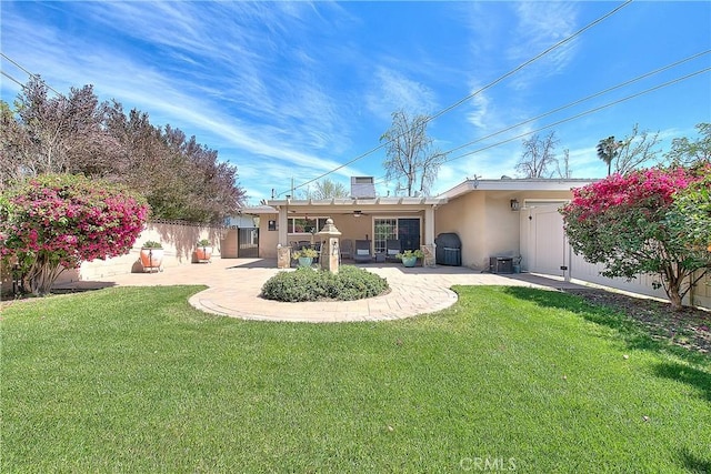 rear view of house featuring a patio, fence, a lawn, and stucco siding