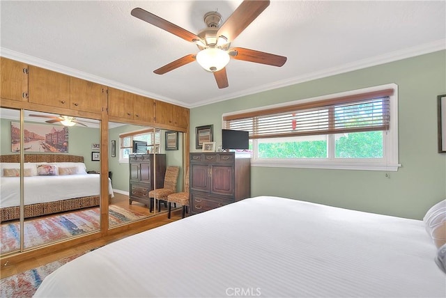 bedroom featuring ornamental molding, wood finished floors, a ceiling fan, and two closets
