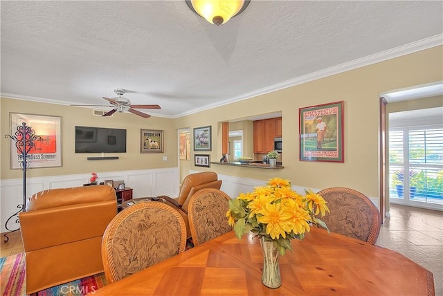 dining area featuring a textured ceiling, a wainscoted wall, ceiling fan, and ornamental molding