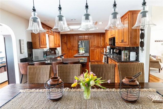 kitchen with dark countertops, stainless steel appliances, arched walkways, recessed lighting, and light wood finished floors