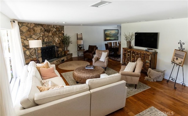 living area featuring visible vents, wood finished floors, and a stone fireplace