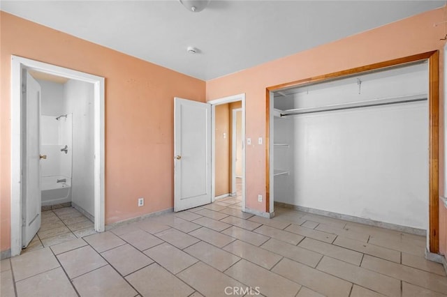 unfurnished bedroom featuring light tile patterned flooring, baseboards, a closet, and ensuite bathroom