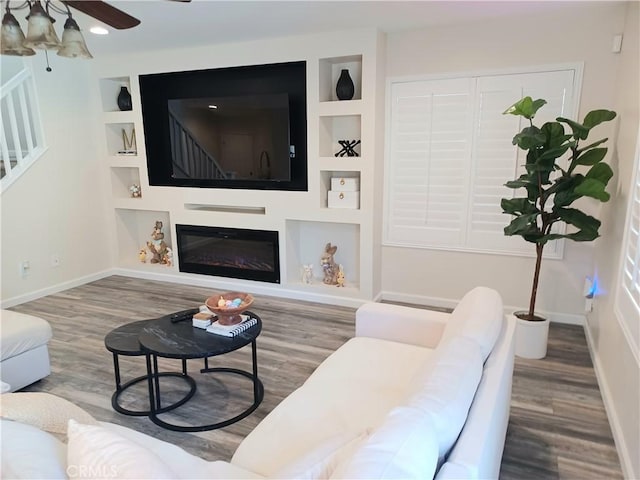 living room featuring stairs, baseboards, ceiling fan, built in features, and wood finished floors