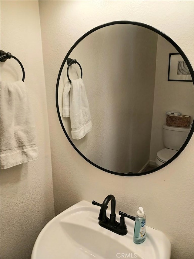 bathroom with a textured wall, a sink, and toilet