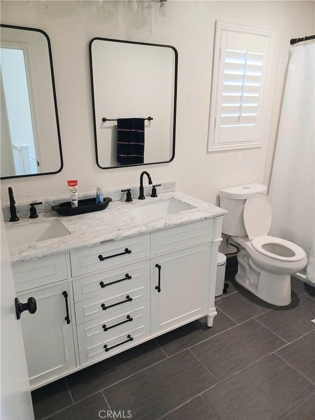 bathroom with toilet, a sink, and double vanity
