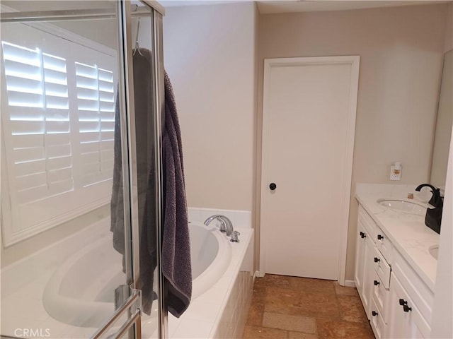full bath with stone finish flooring, double vanity, a sink, a stall shower, and a garden tub