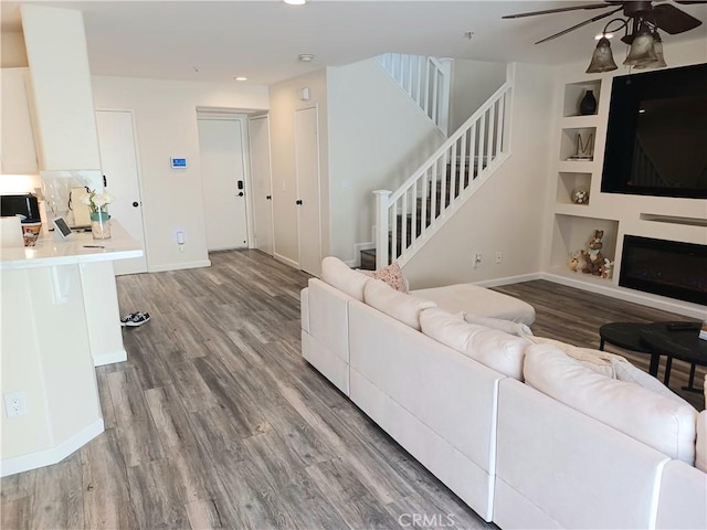 living room with stairway, baseboards, built in shelves, ceiling fan, and wood finished floors