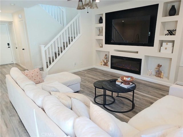 living room with baseboards, built in shelves, stairway, and wood finished floors