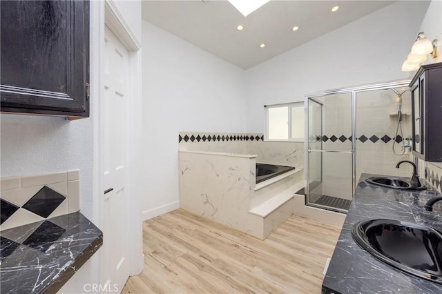 bathroom featuring a shower stall, vaulted ceiling with skylight, wood finished floors, and a sink