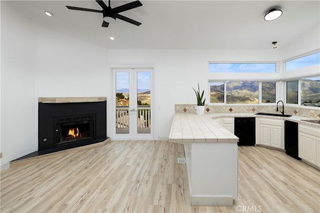 kitchen with white cabinets, a sink, ceiling fan, a peninsula, and tile countertops