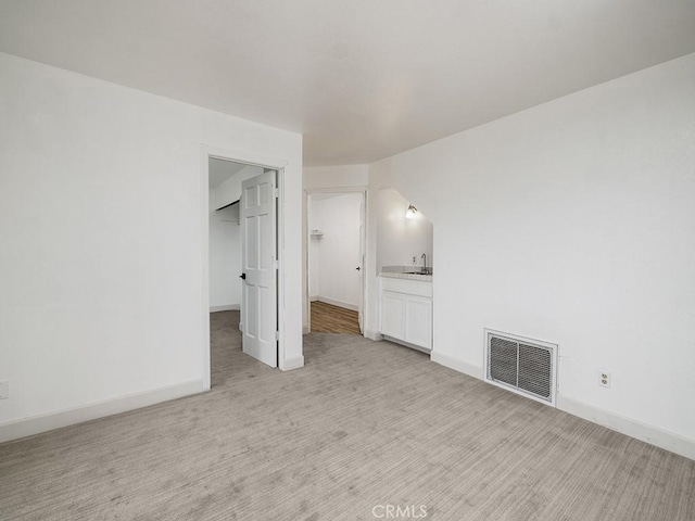 unfurnished bedroom with a spacious closet, visible vents, light carpet, a sink, and baseboards