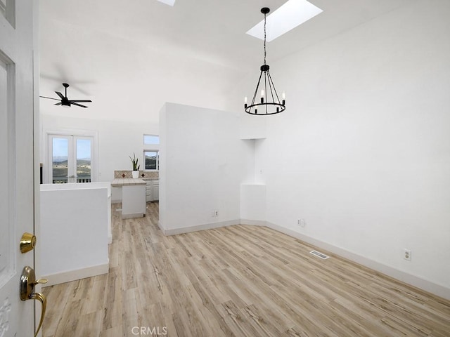 unfurnished dining area featuring ceiling fan with notable chandelier, visible vents, a skylight, light wood finished floors, and baseboards