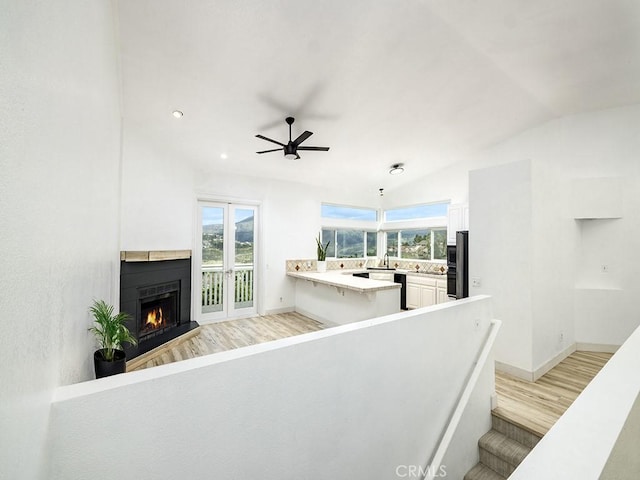 living room with light wood-style floors, vaulted ceiling, a warm lit fireplace, and a wealth of natural light