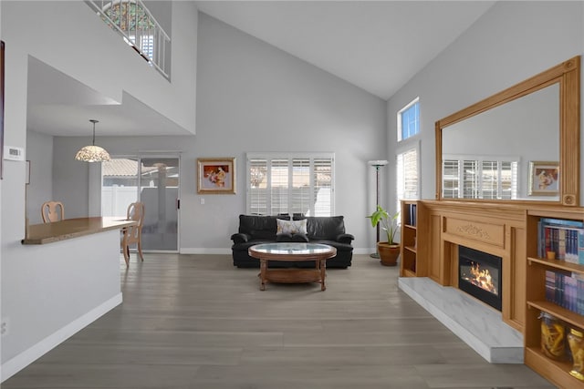 living area featuring high vaulted ceiling, an inviting chandelier, a glass covered fireplace, wood finished floors, and baseboards
