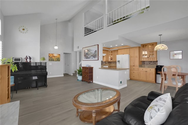 living area with light wood-type flooring, baseboards, and a towering ceiling